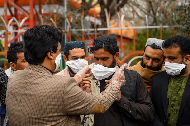 A volunteers (L) hands out free facemasks to people as a preventive measure against the spread of the coronavirus, in Herat city.  AFP