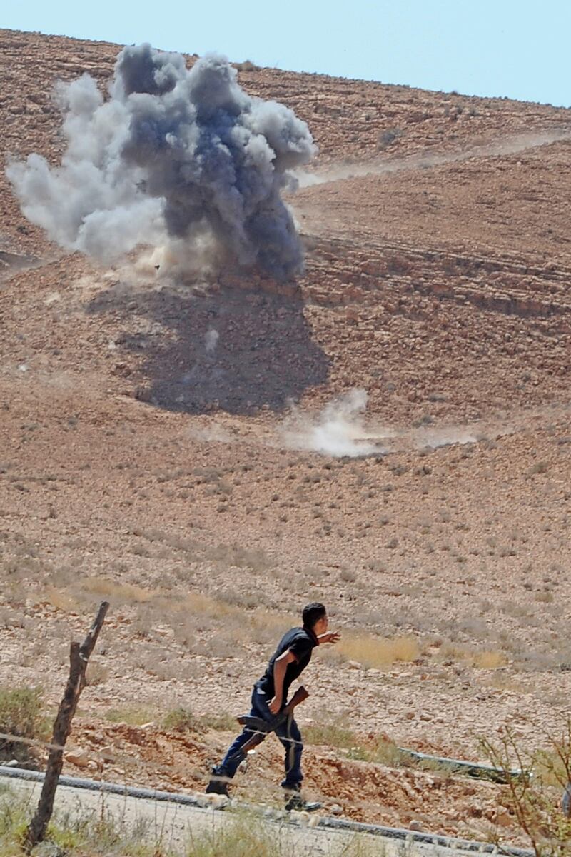 epa02908113 A libyan rebel walks past a smoke rising after the explosion of a Grad rocket launched by Gaddafi troops in Bani Walid now besieged by the rebels, in Libya, 10 September 2011. According to local source, the bombs came just a few yards from the last checkpoint set up by insurgents a few meters from the village where there were also a number of journalists. Street battles raged between the rebels and pro-Gaddafi fighters in the town of Bani Walid, hours after the rebels entered it.  EPA/CIRO FUSCO *** Local Caption ***  02908113.jpg