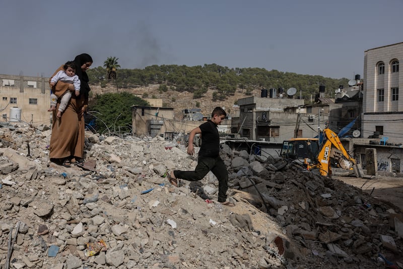 Ayat Abdullah, 31, with her daughter Aylar, one, on the rubble of the building, destroyed by the Israeli army, where she used to have a shop – her sole source of income 