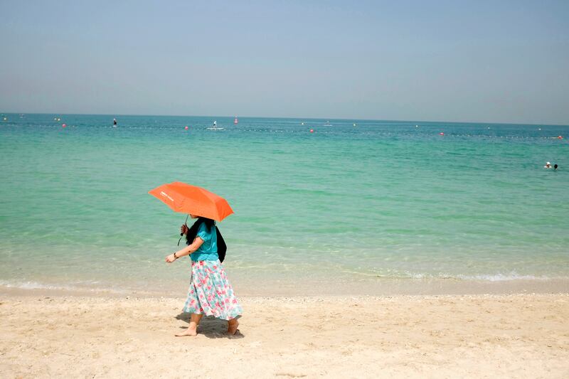 DUBAI, UNITED ARAB EMIRATES, 11 SEPTEMBER 2015. Standalone. A woman shelters from the sun under an umbrella as she walks along the Surf Beach next to Burj Al Arab. (Photo: Antonie Robertson/The National) Journalist: None. Section: National.