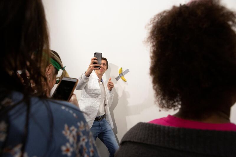 A man poses for a photo next to a banana attached with duct-tape that replaces the artwork 'Comedian' by the artist Maurizio Cattelan, which was eaten by David Datuna, in Miami Beach, Florida, December 7, 2019.  REUTERS/Eva Marie Uzcategui