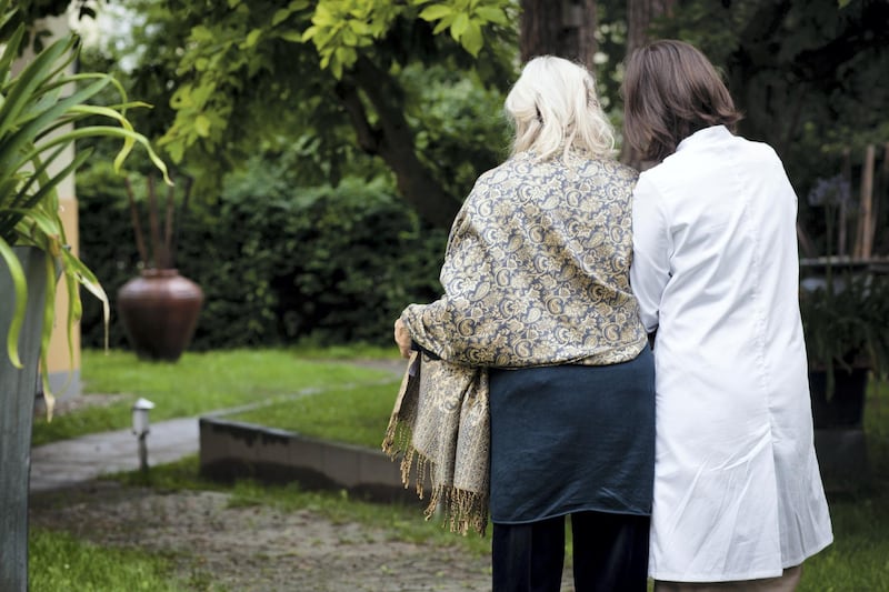 living in old people's home: geriatric nurse helps for a walk  in park