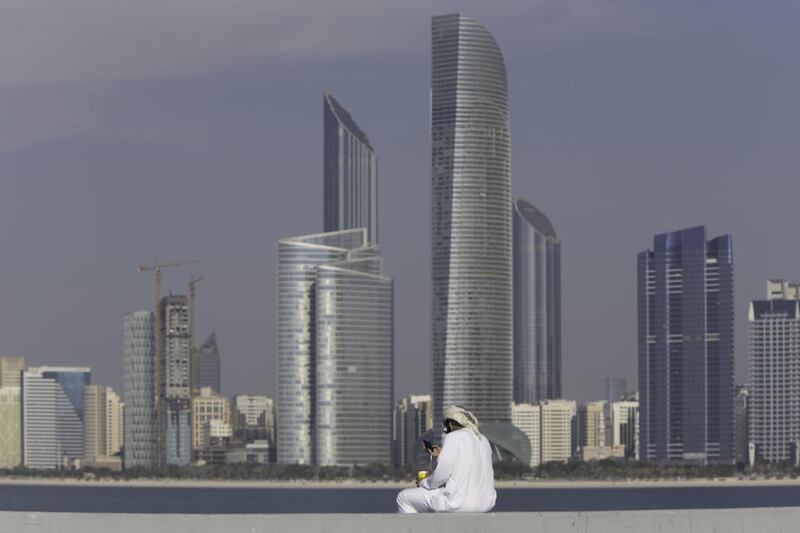 An Emirati man uses his smartphone while drinking coffee on the breakwater along the corniche in Abu Dhabi. Christopher Pike / The National

