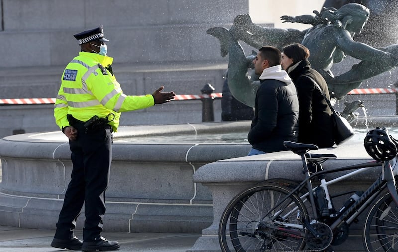 Police speak to pedestrians sitting in Trafalgar Square in London. EPA