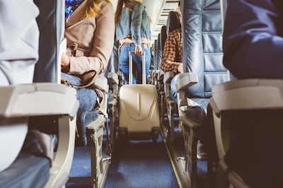 Interior of airplane with people sitting on seats. Passengers with suitcase in aisle looking for seat during flight. Getty Images