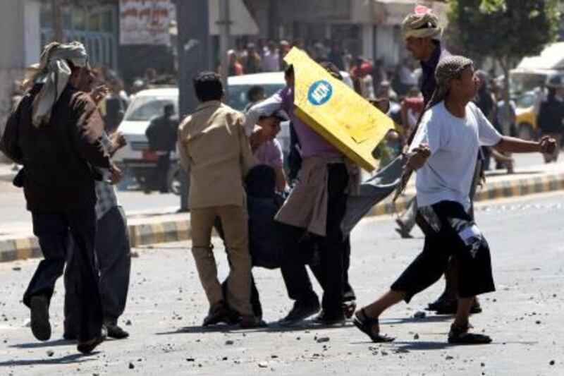 Yemeni anti-government protesters use a makeshift shield to protect a wounded demonstrator during clashes with regime loyalists in central Sanaa on February 17, 2011. At least 12 people were injured and police fired warning shots during the fierce clashes, an AFP reporter said. AFP PHOTO/AHMAD GHARABLI

 *** Local Caption ***  310536-01-08.jpg