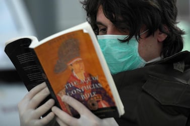 A passenger from Greece with a protective mask reads a book on March 25,2020 at Duesseldorf's airport, western Germany, as the airport remains empty due to the spread of the novel coronavirus COVID-19. After a decade as Europe's leading disciple of fiscal virtue, Germany is unleashing a flood of government cash to counter the devastating economic impact of the novel coronavirus. Airline group Lufthansa has cancelled almost all flights in the coming weeks, while tour operator TUI has already applied for state aid. / AFP / Ina FASSBENDER