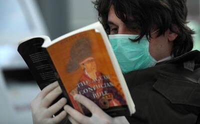 A passenger from Greece with a protective mask reads a book on March 25,2020 at Duesseldorf's airport, western Germany, as the airport remains empty due to the spread of the novel coronavirus COVID-19.  After a decade as Europe's leading disciple of fiscal virtue, Germany is unleashing a flood of government cash to counter the devastating economic impact of the novel coronavirus. Airline group Lufthansa has cancelled almost all flights in the coming weeks, while tour operator TUI has already applied for state aid. / AFP / Ina FASSBENDER
