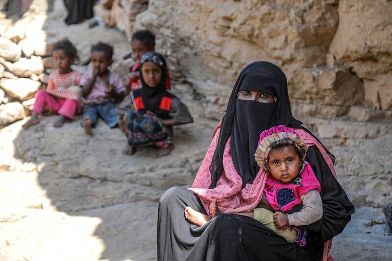 A woman holds a child as she sits near other children outside a cave where a Yemeni family has sought refuge due to poverty and lack of housing, west of the suburbs of Yemen's third-city of Taez on December 2, 2020. (Photo by AHMAD AL-BASHA / AFP)