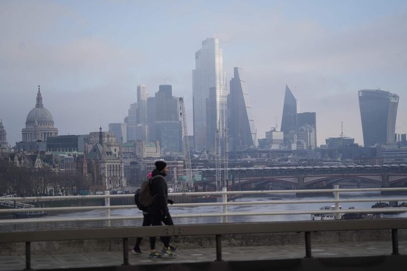 Pedestrians walk along a bridge over the River Thames with skyscrapers and offices of the City of London in the background. AFP