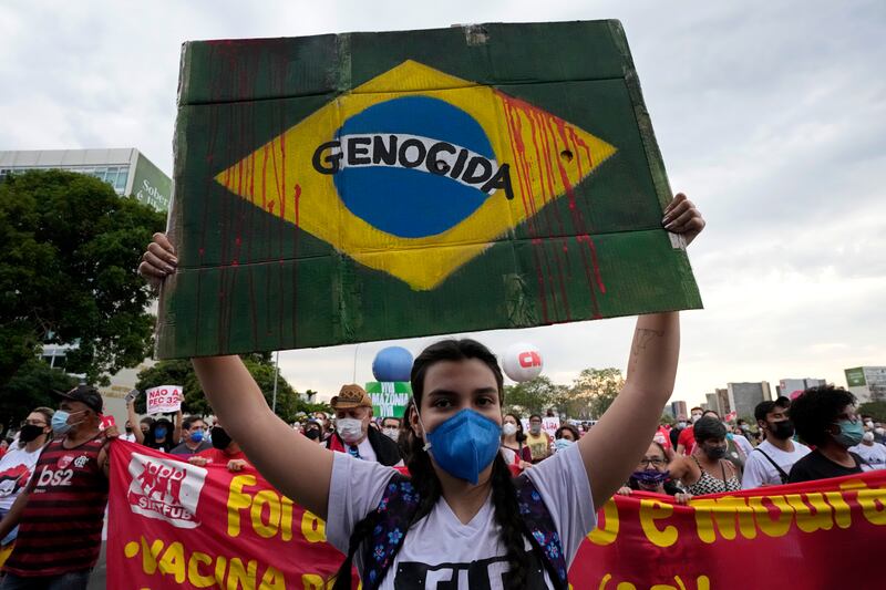 A demonstrator holds up a poster depicting the Brazilian flag with red dripping lines representing blood and the Portuguese word for "Genocide", during a protest against President Jair Bolsonaro. AP.