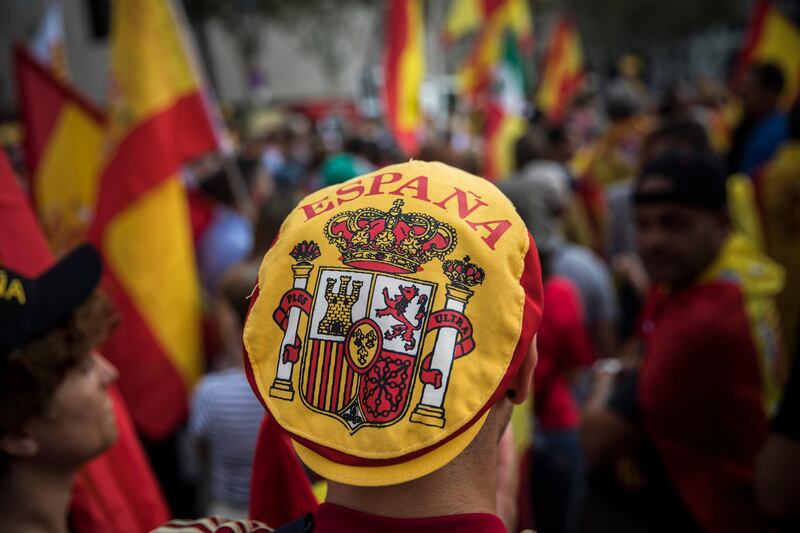 A man wears a hat with the coat of arms of the Spanish flag while people celebrate a holiday known as "Dia de la Hispanidad" or Spain's National Day in Barcelona, Spain, Thursday, Oct. 12, 2017. Spain's celebrates its national day amid one of the country's biggest crises ever as its powerful northeastern region of Catalonia threatens independence. (AP Photo/Santi Palacios)