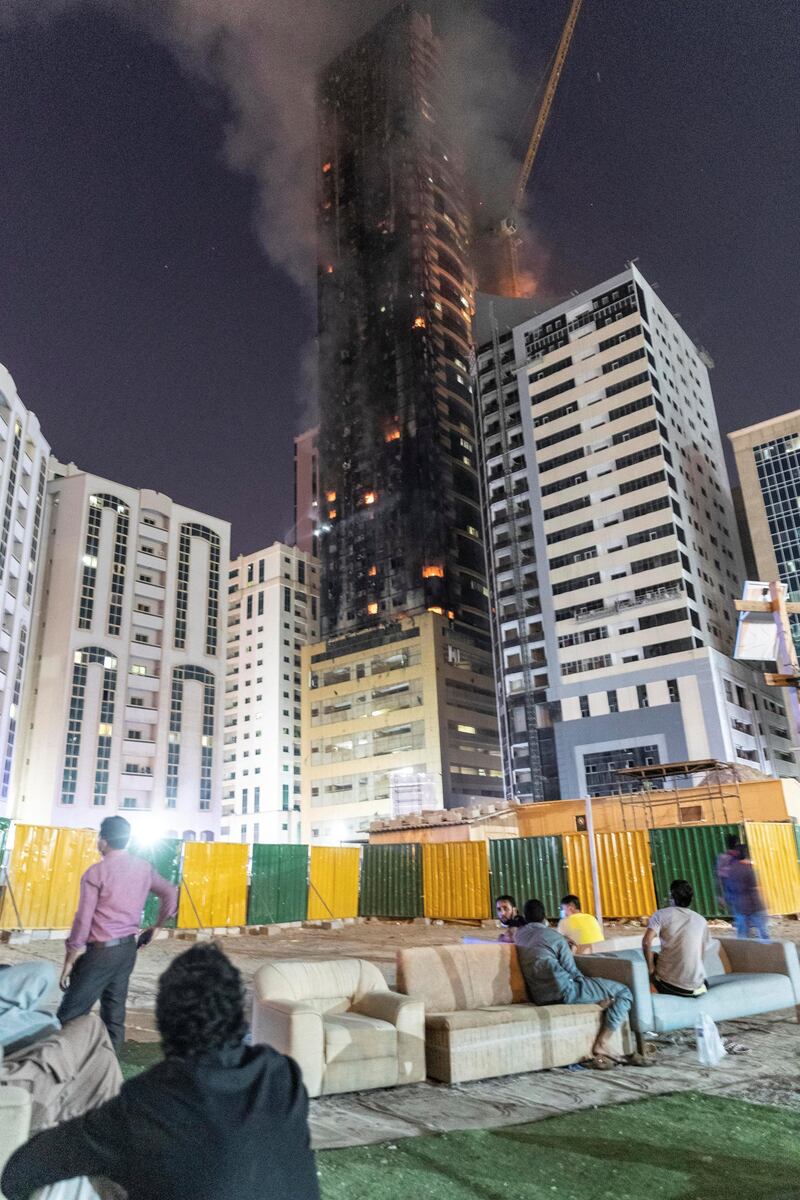 SHARJAH, UNITED ARAB EMIRATES. 05 MAY 2020. STANDALONE. Fire at the Abbco Tower near Nahda Park in Sharjah. Police and fire fighters responded to a blaze that was reported after 8:30. Men sit and watch the fire. (Photo: Antonie Robertson/The National) Journalist: Salam Al Amir. Section: National.