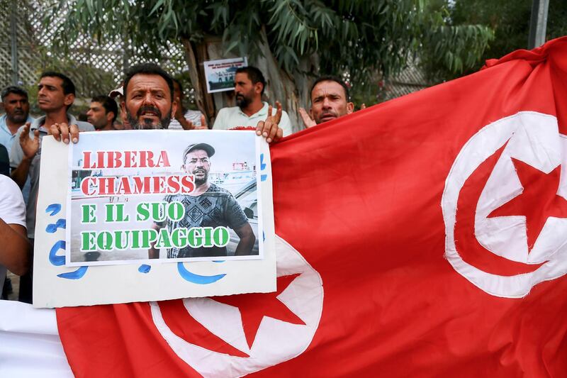 A Tunisian fisherman raises a sign next to a make-shift Tunisian flag during a protest outside the Italian embassy in the capital Tunis on September 6, 2018, calling for their release after being arrested by Italian authorities earlier in the week for rescuing African migrants in international waters and taking them to Italy. (Photo by ANIS MILI / AFP)