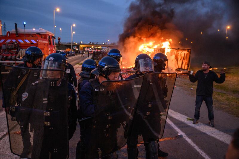 French police officers stand guard near a burning vehicle during a farmers' protest against taxation and declining income, in the southern town of Narbonne.  AFP
