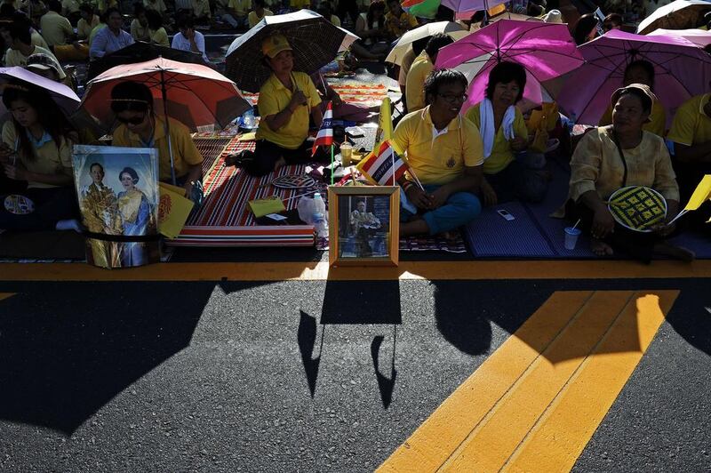 Well-wishers sit by portraits of Thai King Bhumibol Adulyadej and Queen Sirikit as they line up along the road leading to the Royal Palace where the King later marked the 64th anniversary of his coronation, in the seaside city of Hua Hin some 200 kilometres south of Bangkok. Christophe Archambault / AFP Photo