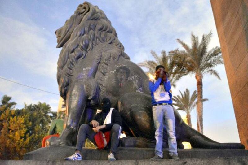 A member of Egypt's Black Bloc anarchic group (L) and a protestor rest under a lion statue on CairoÕs Qasr al-Nil bridge during clashes with riot police near Cairo's Tahrir Square on January 28, 2013. Egypt's main opposition bloc rejected an invitation by President Mohamed Morsi for talks on the violence and political turmoil sweeping the country and instead called for fresh mass demonstrations. AFP PHOTO / KHALED DESOUKI

