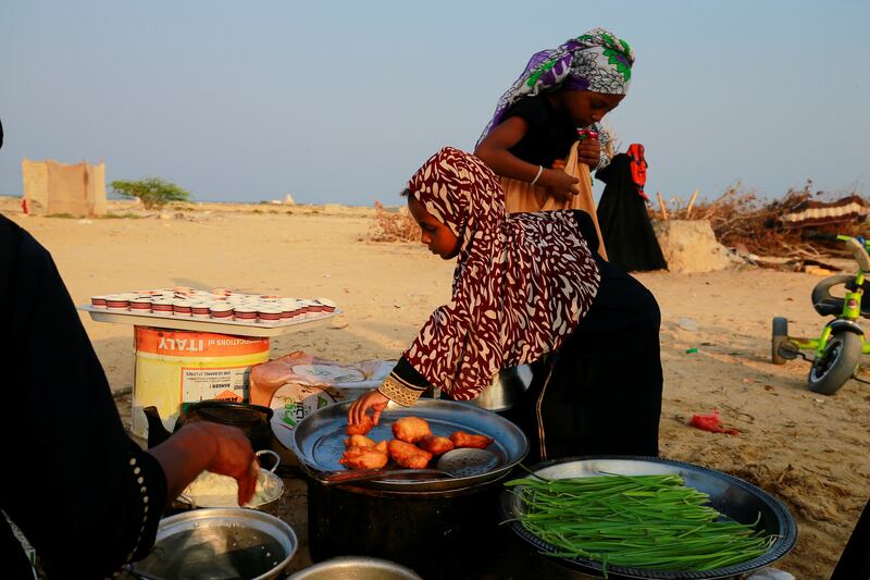 A girl picks food prepared by her mother at a camp for displaced people in Al Ghaidha.