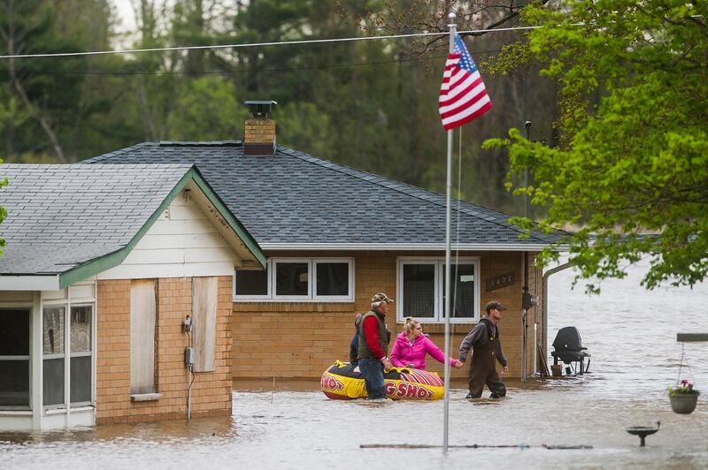 People help each other travel from one home to another using an inflatable raft on Oakridge Road on Wixom Lake. Midland Daily News via AP