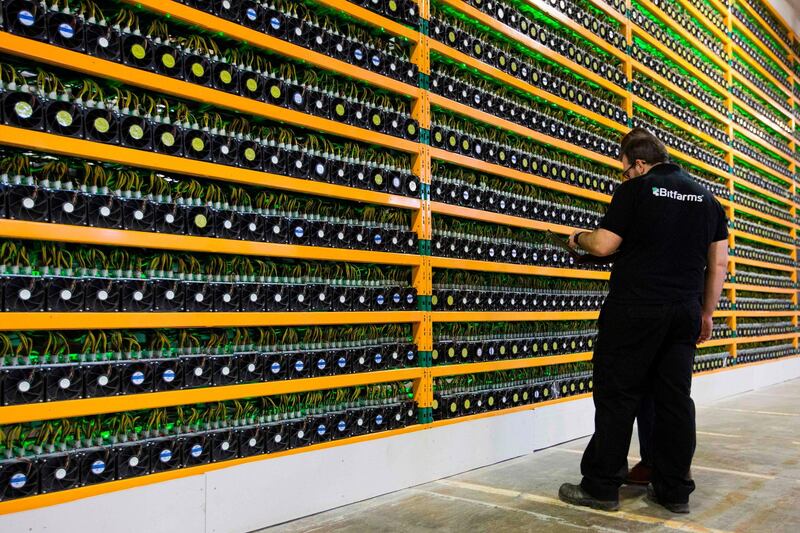 (FILES) In this file photo taken on March 19, 2018 two technicians inspect bitcoin mining at Bitfarms in Saint Hyacinthe, Quebec. - In his apartment, Ali accumulates rigs to mine for cryptocurrencies though the benefits are less than what he thought due to the fall in prices. (Photo by Lars Hagberg / AFP) / TO GO WITH AFP STORY by KEVIN TRUBLET