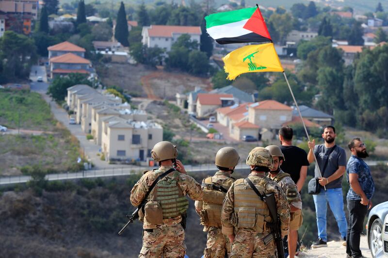 Lebanese soldiers stand on a hill overlooking the Israeli town of Metula, as a man waves the Palestinian and Hezbollah flags, in Kfar Kila, southern Lebanon, on Monday. So far, there have been only limited exchanges between the Israeli military and Hezbollah amid the violence in Gaza. AP