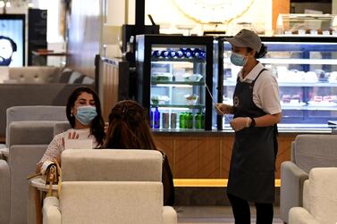 Women wearing masks for protection against the coronavirus, sit at a restaurant in the Mall of Dubai on April 28, 2020, after the shopping centre was reopened as part of moves in the Gulf emirate to ease lockdown restrictions imposed last month to prevent the spread of the COVID-19 illness. / AFP / Karim SAHIB