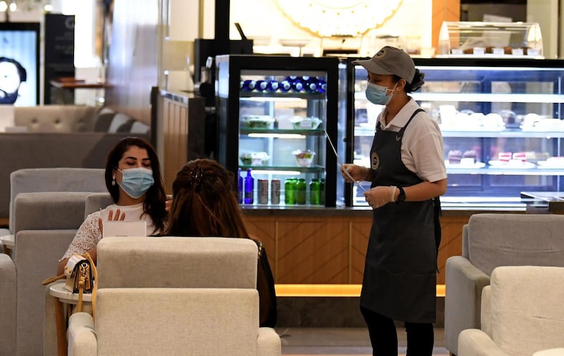 Women wearing masks for protection against the coronavirus, sit at a restaurant in the Mall of Dubai on April 28, 2020, after the shopping centre was reopened as part of moves in the Gulf emirate to ease lockdown restrictions imposed last month to prevent the spread of the COVID-19 illness.  / AFP / Karim SAHIB
