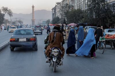 An armed Taliban fighter passes women in burqas in Kabul, Afghanistan in 2021. Reuters