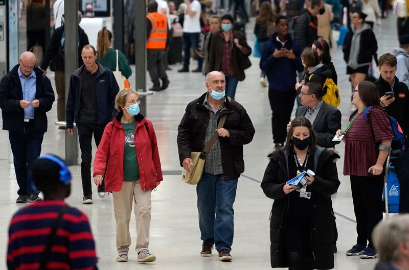 Commuters, some wearing face coverings, walk through Waterloo train station in central London.