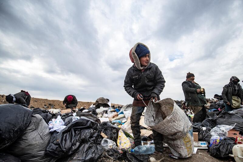 Syrians sift through a garbage dump in the countryside of Malikiya in northeast Syria, on January 17, 2021. - On the dry plains outside the city of Al-Malikiyah, a dozen people wrapped up against the cold rip open the black plastic bags, in a desperate search for something to sell, repurpose or even eat. Across the road, an oil pump swings back and forth in this resource-rich region controlled by US-backed Kurdish forces. (Photo by Delil SOULEIMAN / AFP)