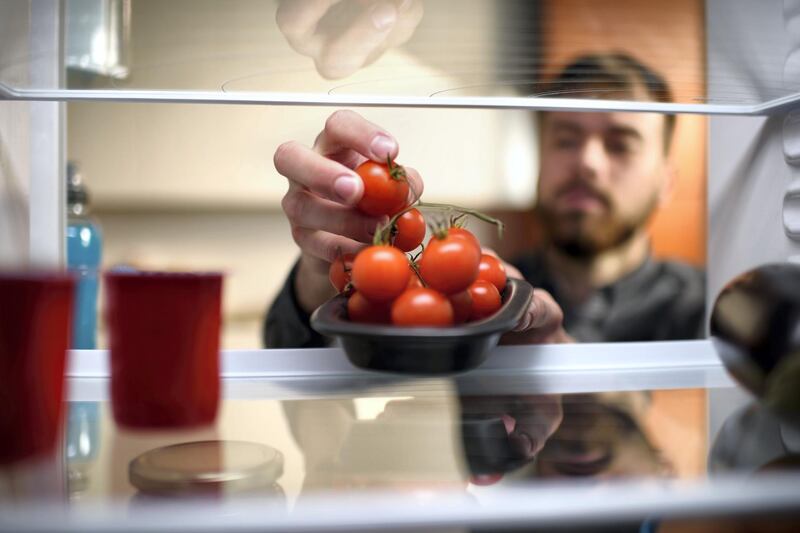 Man picking up cherry tomatoes from the refrigerator.