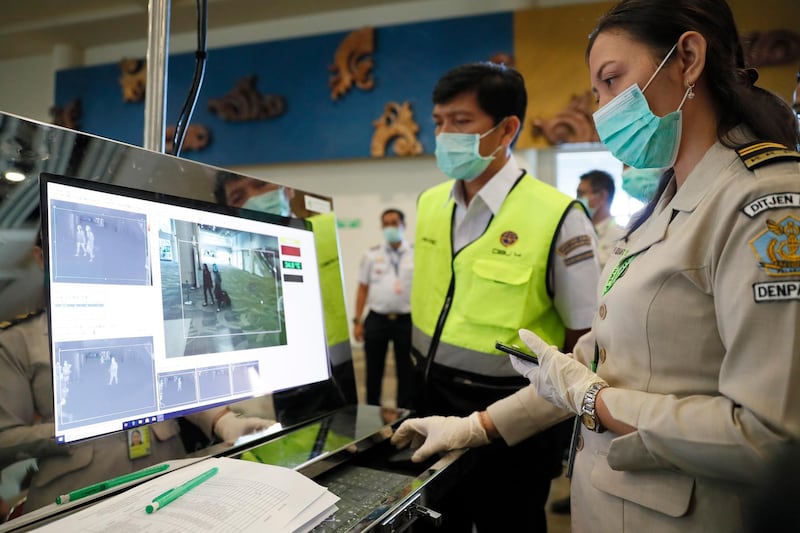 An officer inspects a monitor as passengers walk through a thermal scanner upon their arrival at Ngurah Rai International Airport in Kuta, Bali, Indonesia.  EPA