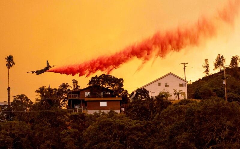 TOPSHOT - An airplane drops fire retardant over homes in the Spanish Flat area of Napa, California as flames rage through on August 18, 2020. As of the late hours of August 18, the Hennessey fire has merged with at least 7 fires and is now called the LNU Lightning Complex fires. Dozens of fires are burning out of control throughout Northern California as fire resources are spread thin. / AFP / JOSH EDELSON
