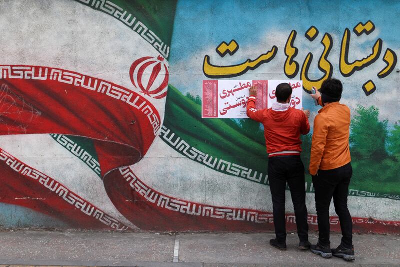 Men put posters on a wall during the last day of election campaigning, in Tehran. Reuters