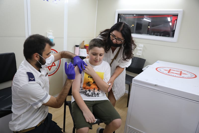 12-year-old Yonatan Rosh receives a Covid-19 vaccine as he is support by his mother Ilana at a vaccines station in Tel Aviv.