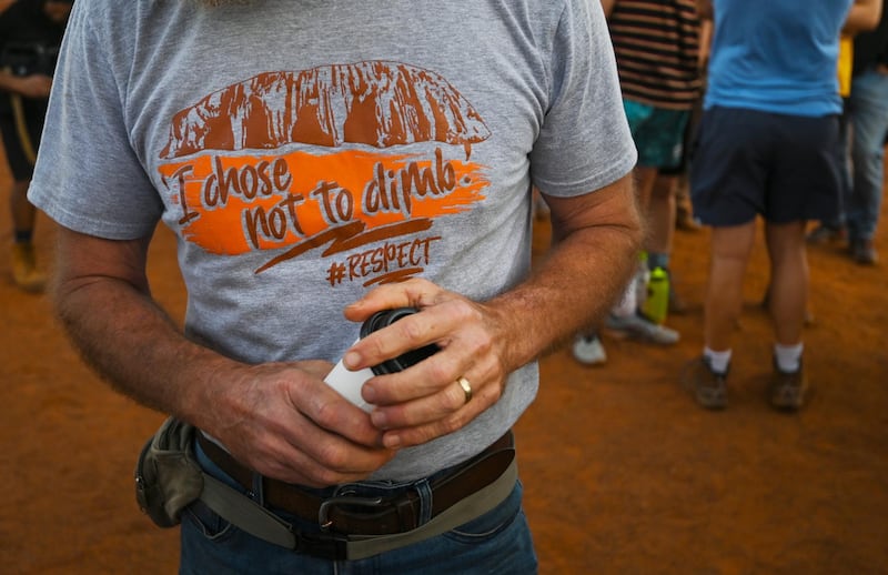 A man wearing a t-shirt saying 'I chose not to climb' stands next to tourists lining up to climb Uluru. EPA