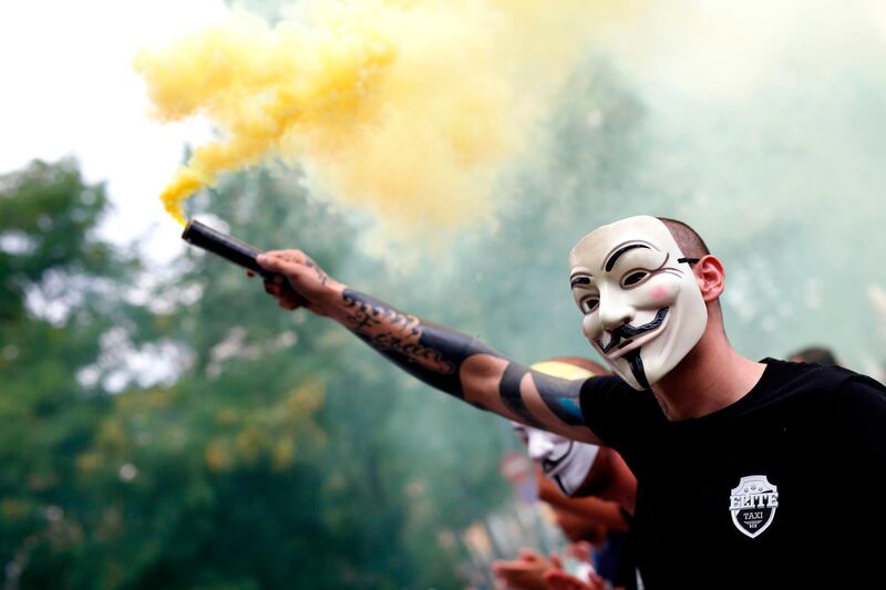 A protester wearing a Guy Fawkes mask lights a flare during a strike by taxi drivers in Barcelona.  AFP / Pau Barrena