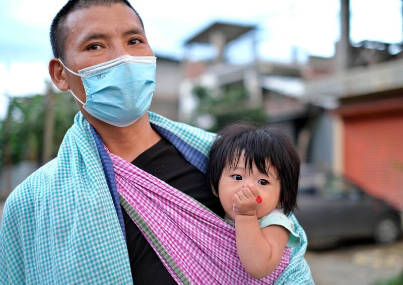 A man wearing a face mask walks with an infant on a sling in north-east Indian city of Imphal. AP Photo