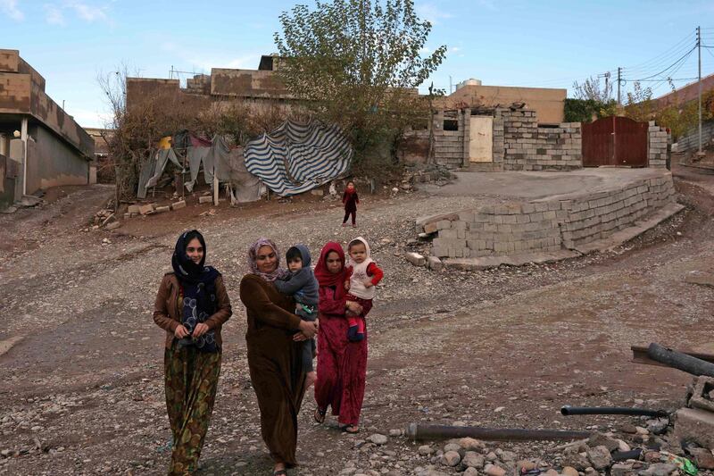 Iraqi women carry children as they walk in Sharboty Saghira, a small village east of regional capital Arbil. FP