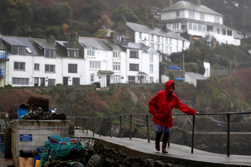 A woman holds a hand rail to steady herself as she walks along the harbour wall in Polperro, south west England, as Storm Ciara swept over the country.  AFP