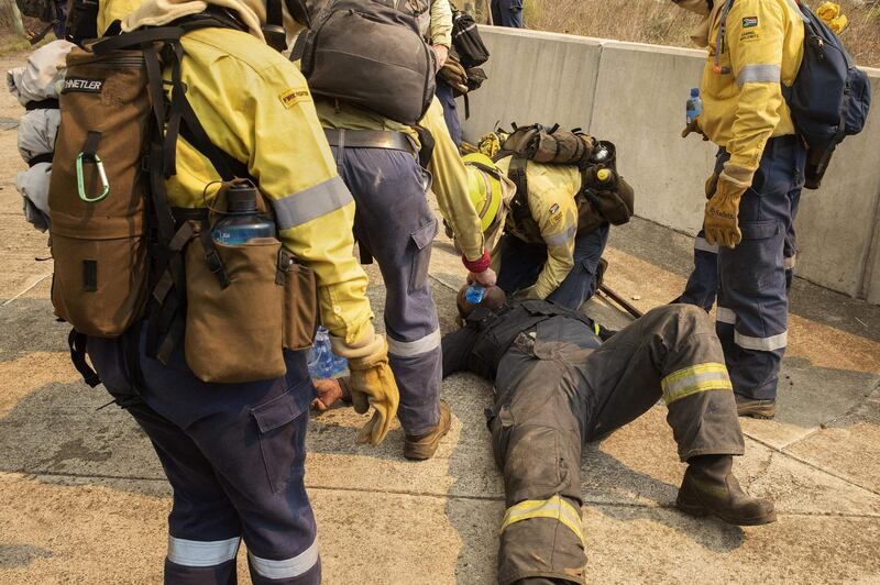 Colleagues attend to a firefighter who collapsed due to the effects of smoke and heat, while fighting the forest fire on the foothills of Table Mountain. AFP