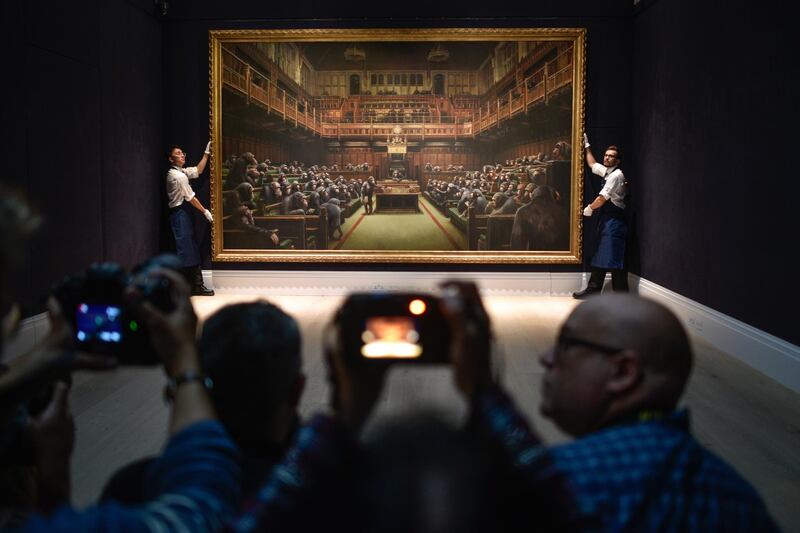 Gallery assistants pose with the Banksy painting 'Devolved Parliament' at Sotheby's in London, England. Getty