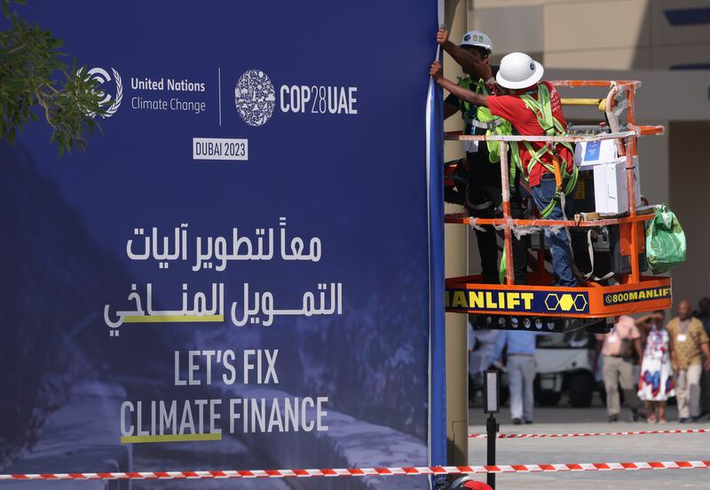 Workers prepare a banner that reads 'Let's Fix Climate Finance' ahead of the official opening of Cop28 in Dubai. Getty Images