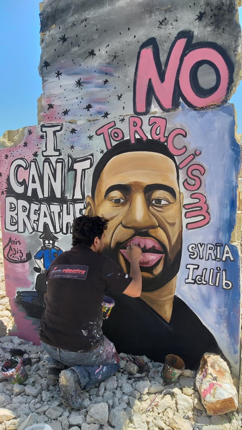 Aziz Asmar painting a mural of George Floyd on a destroyed building wall in Idlib, Syria, with the words 'I can't breathe' and 'No to racism'. Aziz Asmar