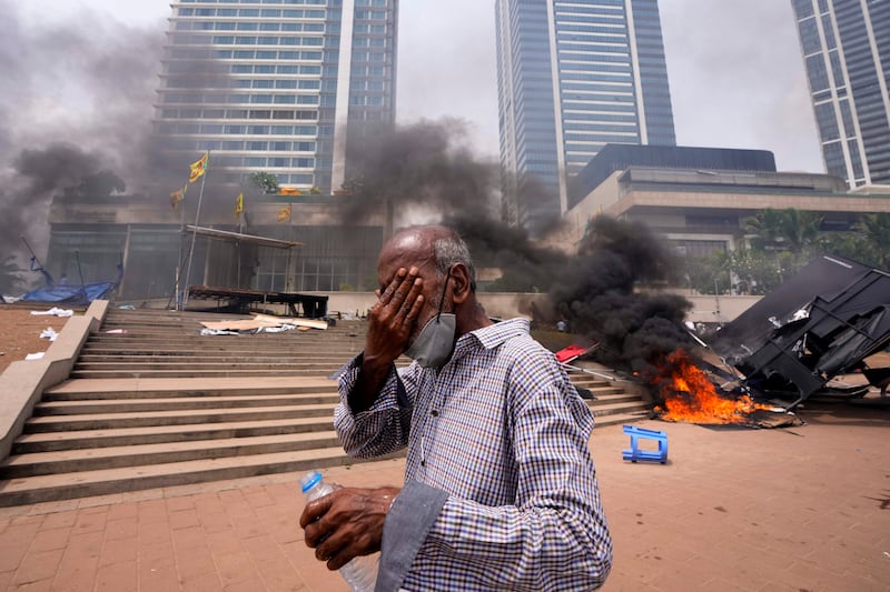 A man suffers after being sprayed with tear gas as cars burn on the streets of Colombo, Sri Lanka. AP