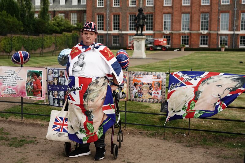A royal fan poses by the the gates outside Kensington Palace, surrounded by tributes to Princess Diana. PA