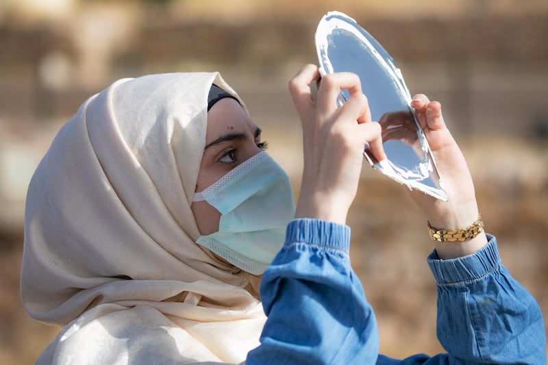A woman wearing a face mask uses a mirror covered with a special filter to observe a partial solar eclipse at the Citadel in downtown Amman, Jordan. EPA