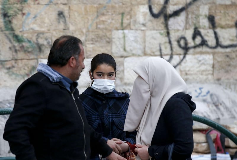 A Palestinian girl wearing a protective mask waits as her relatives chat on a street in the West Bank city of Hebron amid fears of the spread of the novel coronavirus.  AFP