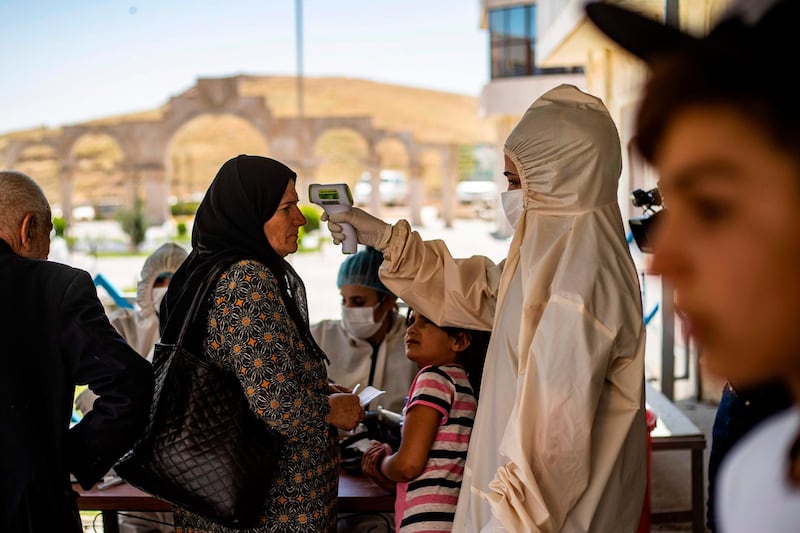 A medic checks the body temperature of passengers, who were stranded following the closure of border upon their arrival from Iraqi Kurdistan to the Syrian side of the Semalka border crossing in north-east Syria. AFP