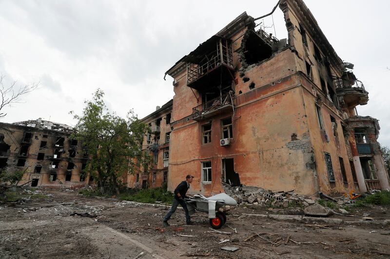 A man pushes a wheelbarrow past a heavily damaged apartment building near Azovstal Iron and Steel Works in Mariupol. Reuters